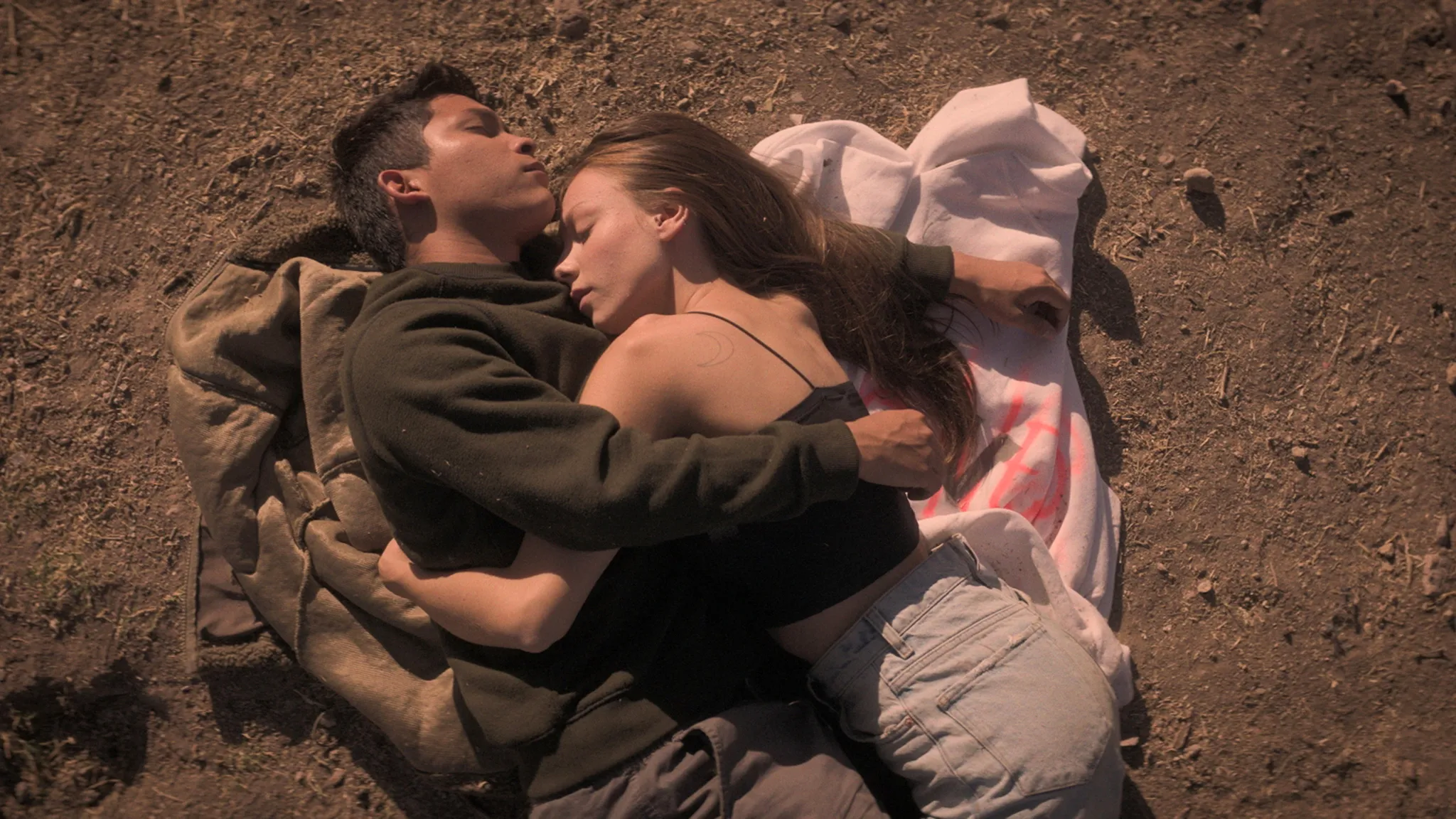Couple laying on a blanket on a beach, sleeping and hugging.