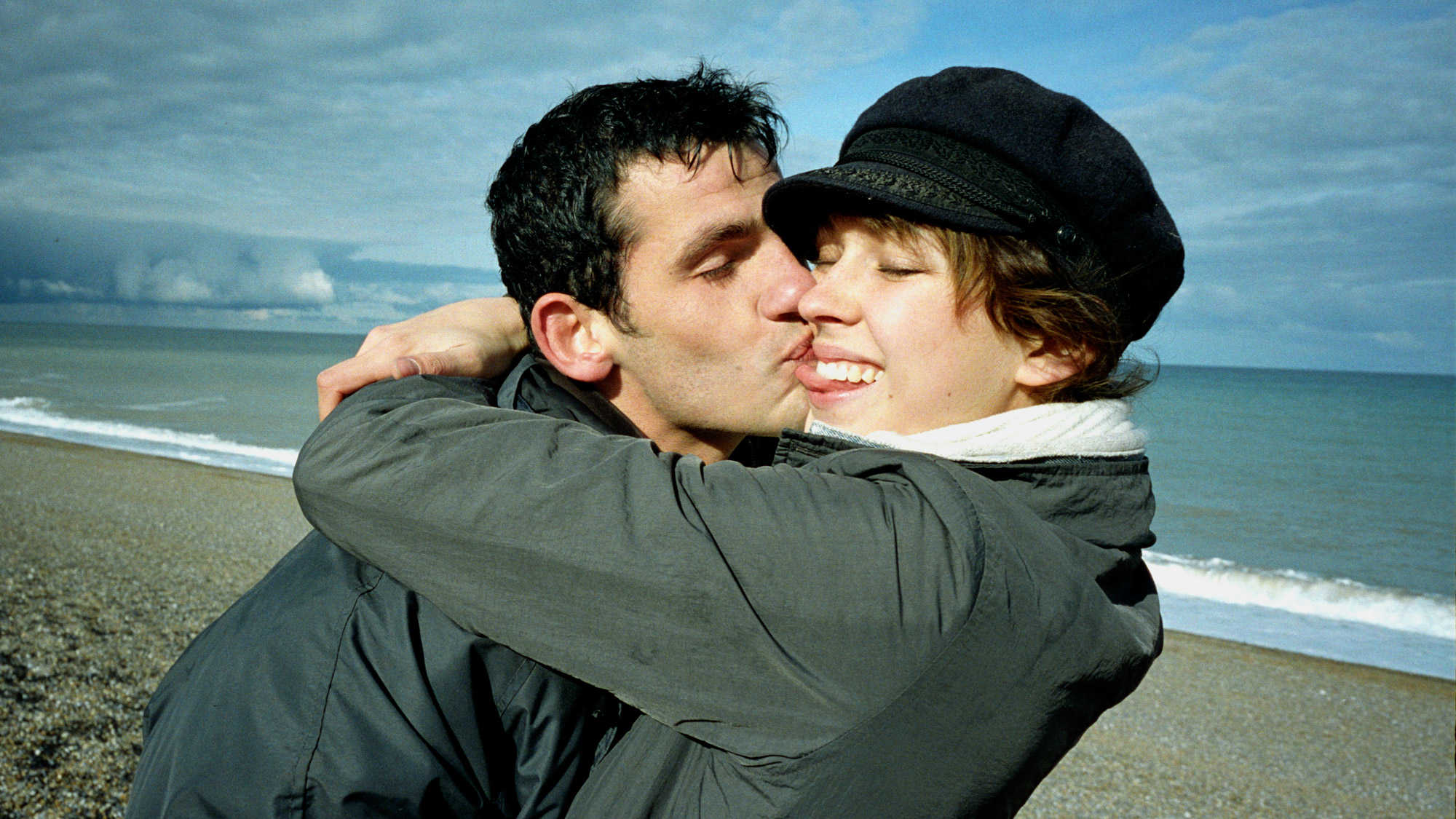 Een koppel dat elkaar knuffelt en kust op een zonnige, schijnbaar koude dag op het strand.